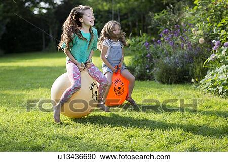 Stock Image - Two sisters bouncing on bouncy hoppers. Fotosearch