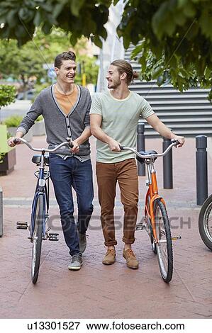 Two young men pushing bicycles View Large Photo Image Stock Photo - Two young men pushing bicycles. Fotosearch