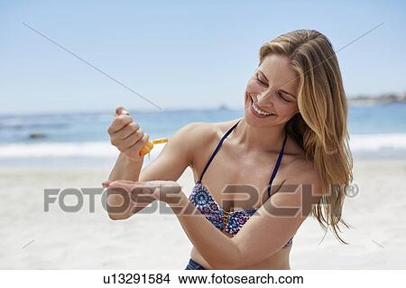 Picture - Woman applying sun cream on beach. Fotosearch