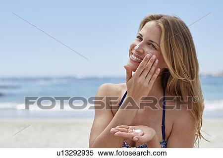 Stock Photography - Woman applying sun cream on beach. Fotosearch