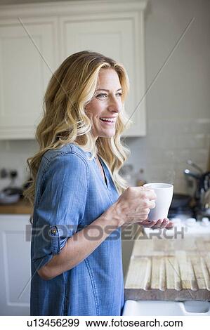 Woman in kitchen with hot drink, portrait View Large Photo Image Stock Photo - Woman in kitchen with hot drink, portrait. Fotosearch