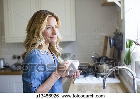 Stock Photograph - Woman in kitchen with hot drink, portrait. Fotosearch