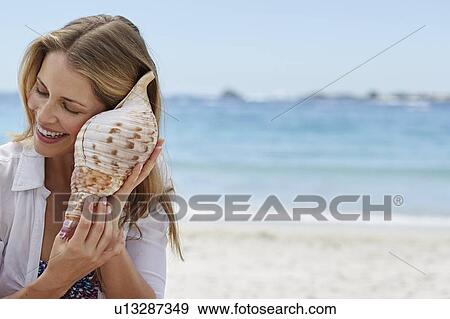 Woman listening to a seashell View Large Photo Image Stock Photo - Woman listening to a seashell. Fotosearch