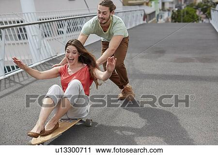 Woman on skateboard, man pushing View Large Photo Image Stock Image - Woman on skateboard, man pushing. Fotosearch