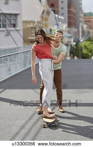 Stock Photograph - Woman skateboarding with man pushing. Fotosearch