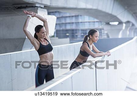 Stock Photo - Woman stretching, friend leaning on wall. Fotosearch