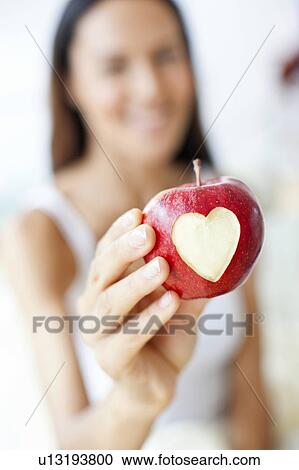 Stock Image - Young woman holding apple with heart. Fotosearch