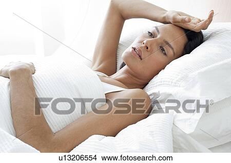 Picture - Young woman in bed with hand on forehead. Fotosearch
