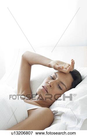 Young woman in bed with hand on forehead View Large Photo Image Stock Photo - Young woman in bed with hand on forehead. Fotosearch