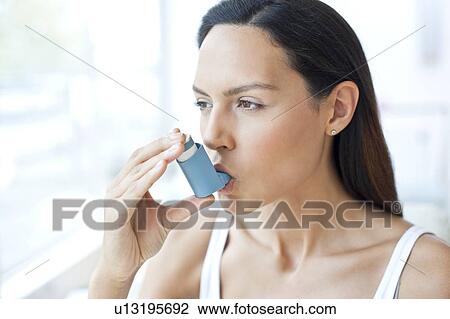 Stock Image - Young woman using inhaler. Fotosearch