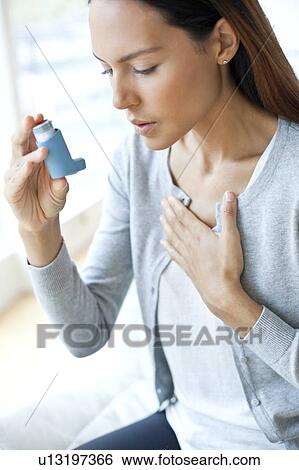 Stock Photograph - Young woman using inhaler touching chest. Fotosearch