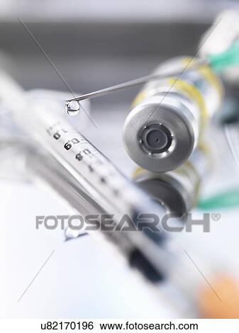 Stock Photograph - Ampoule containing a drug dose next to a syringe with a droplet of medicine at the end of the needle. Fotosearch