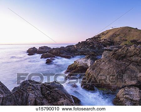 Stock Image - Australia, New South Wales, Port Macquarie, Lighthouse on rocky coat at sunrise. Fotosearch