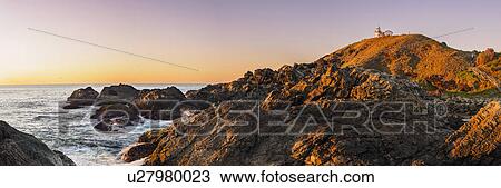 Stock Image - Australia, New South Wales, Port Macquarie, Lighthouse on rocky coat at sunrise. Fotosearch