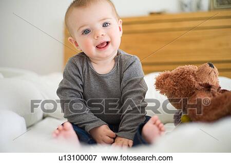 Stock Photo - Baby girl sitting on bed looking at camera. Fotosearch