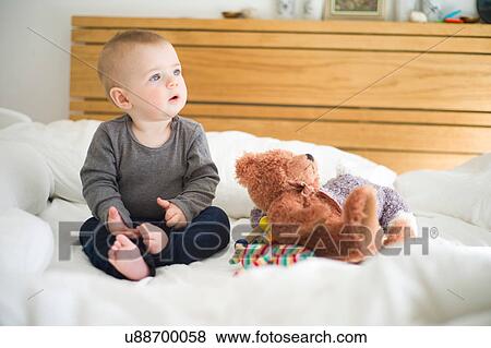 Baby girl sitting on bed with teddy bear looking away View Large Photo Image Stock Photo - Baby girl sitting on bed with teddy bear looking away. Fotosearch