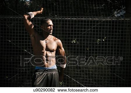 Bare-chested muscular young man posing by wire fence View Large Photo Image Stock Image - Bare-chested muscular young man posing by wire fence. Fotosearch