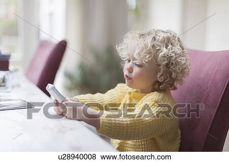 Stock Photo - Blond girl (4-5) sitting at table and looking at mobile phone. Fotosearch