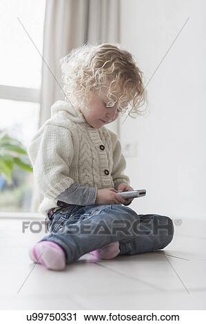 Blond girl (4-5) sitting on floor and playing with mobile phone View Large Photo Image Stock Image - Blond girl (4-5) sitting on floor and playing with mobile phone. Fotosearch