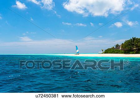 Stock Image - Blue ocean, sailboat on beach, Maldives. Fotosearch