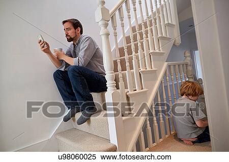 Stock Photography - Boy and father sitting on staircase, father reading smartphone texts. Fotosearch