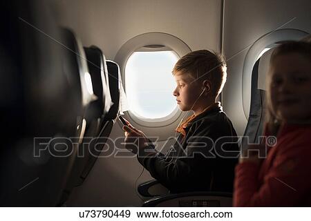 Boy in airplane cabin selecting smartphone music for earphones View Large Photo Image Stock Photo - Boy in airplane cabin selecting smartphone music for earphones. Fotosearch