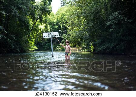 Stock Image - Boy knee deep in water holding stick, France. Fotosearch