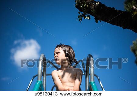 Stock Image - Boy on top of playground slide looking away. Fotosearch