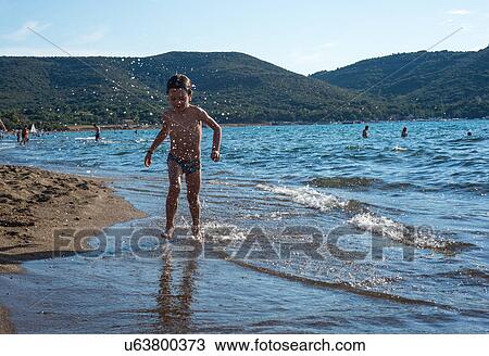 Stock Image - Boy paddling in lapping waves on coastline, Italy. Fotosearch