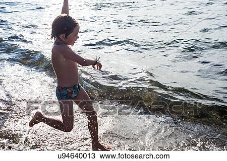 Boy paddling in lapping waves on coastline View Large Photo Image Stock Image - Boy paddling in lapping waves on coastline. Fotosearch