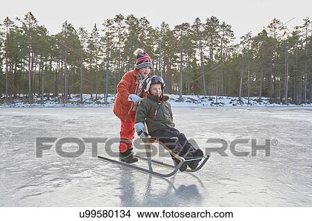 Picture - Boy pushing friend on kicksled across frozen lake, Gavle, Sweden. Fotosearch