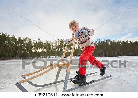 Stock Image - Boy pushing kicksled across frozen lake, Gavle, Sweden. Fotosearch