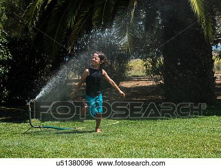 Boy running through water from garden sprinkler View Large Photo Image Stock Photograph - Boy running through water from garden sprinkler. Fotosearch