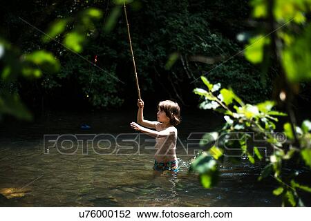 Stock Image - Boy waist deep in water holding stick. Fotosearch