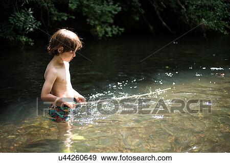 Stock Photo - Boy waist deep in water holding stick. Fotosearch