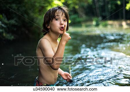 Stock Image - Boy waist deep in water with finger on lips. Fotosearch