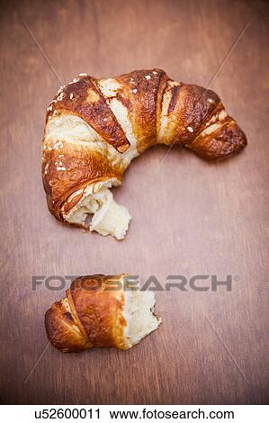 Stock Image - Broken croissant on wooden table. Fotosearch