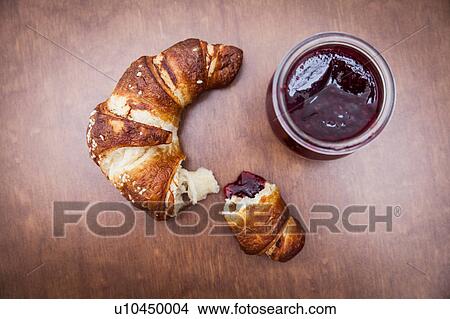 Picture - Broken croissant on wooden table with jam. Fotosearch