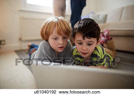 Stock Image - Brothers playing laptop game on room rug. Fotosearch