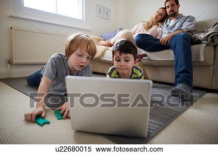 Brothers playing laptop game on room rug, parents on sofa View Large Photo Image Stock Photography - Brothers playing laptop game on room rug, parents on sofa. Fotosearch