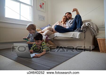 Stock Image - Brothers playing on living room rug, parent on sofa. Fotosearch
