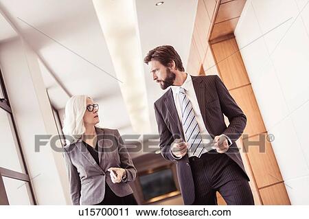 Stock Image - Businessman and woman walking and talking in office corridor. Fotosearch