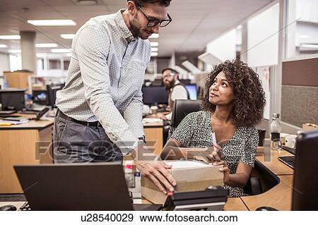 Stock Photo - Businessman handing package to businesswoman in office. Fotosearch