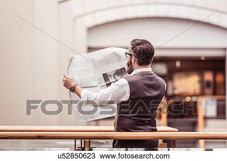 Stock Image - Businessman reading newspaper on office balcony. Fotosearch