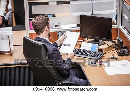 Stock Photo - Businessman reading paperwork at office desk. Fotosearch