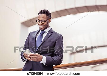 Stock Image - Businessman reading smartphone update on office balcony. Fotosearch
