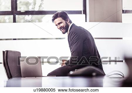 Stock Photography - Businessman sitting on boardroom table laughing. Fotosearch