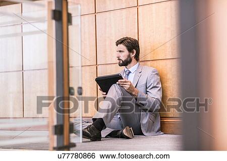 Stock Photograph - Businessman sitting on office floor using digital tablet. Fotosearch