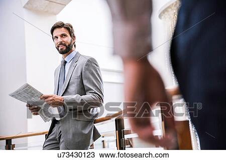 Stock Image - Businessman waiting with newspaper on office balcony. Fotosearch
