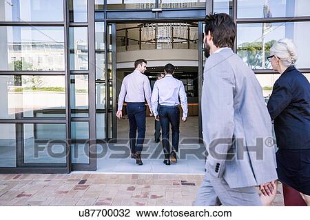 Stock Image - Businessmen and woman arriving at office building. Fotosearch